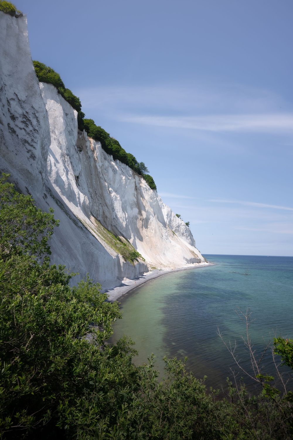 Towering white chalk cliffs of Mons Klint rising above clear turquoise Baltic Sea waters.