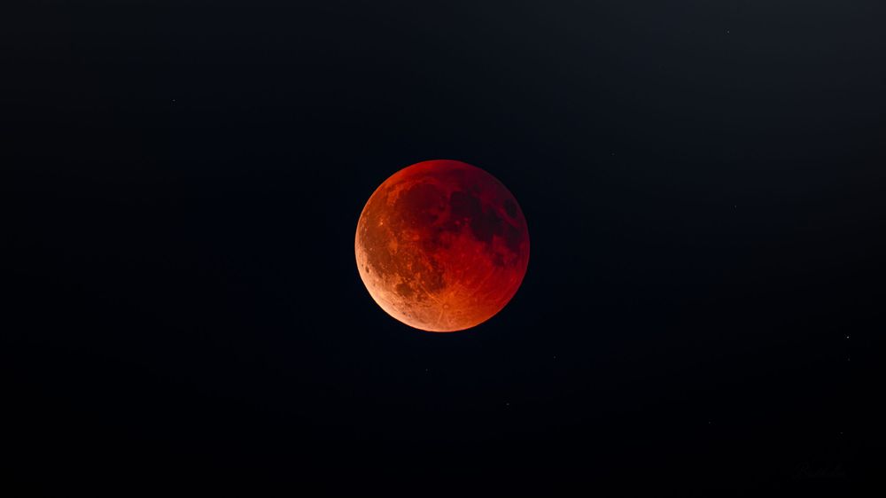 A dramatic blood moon lunar eclipse glowing vivid red and orange against a dark night sky.