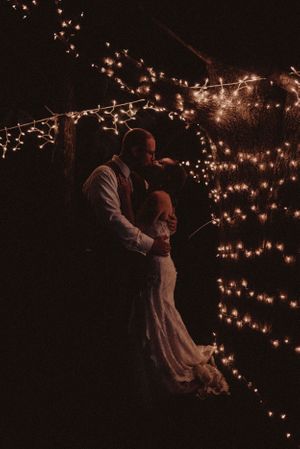 A romantic nighttime dance under twinkling string lights creating a magical ambiance at an outdoor wedding.