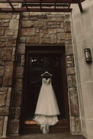 White wedding dress hanging on wooden door of stone building with elegant lighting.