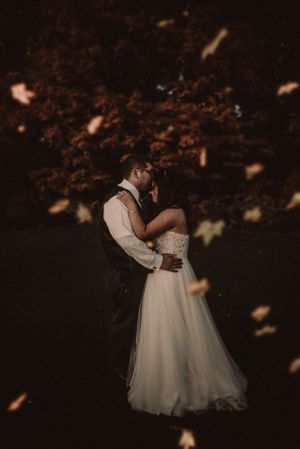 Romantic silhouette of couple dancing in formal wear with falling autumn leaves.