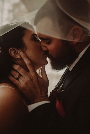 Intimate moment captured under a wedding veil as couple shares a romantic kiss.