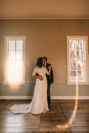 A romantic wedding portrait in a sunlit room with wooden floors and bright windows.