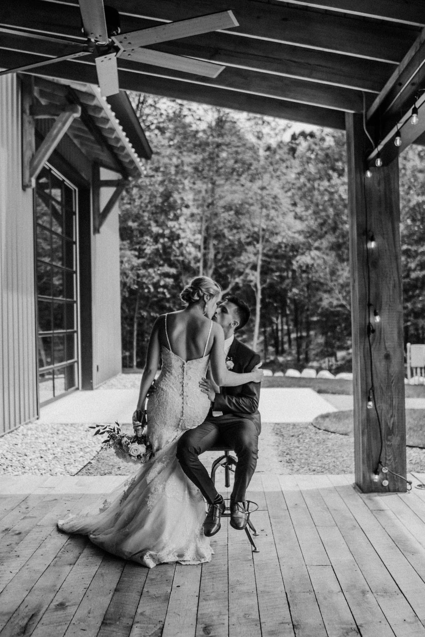 A romantic black and white photo of a couple sharing a moment on a covered wooden deck.