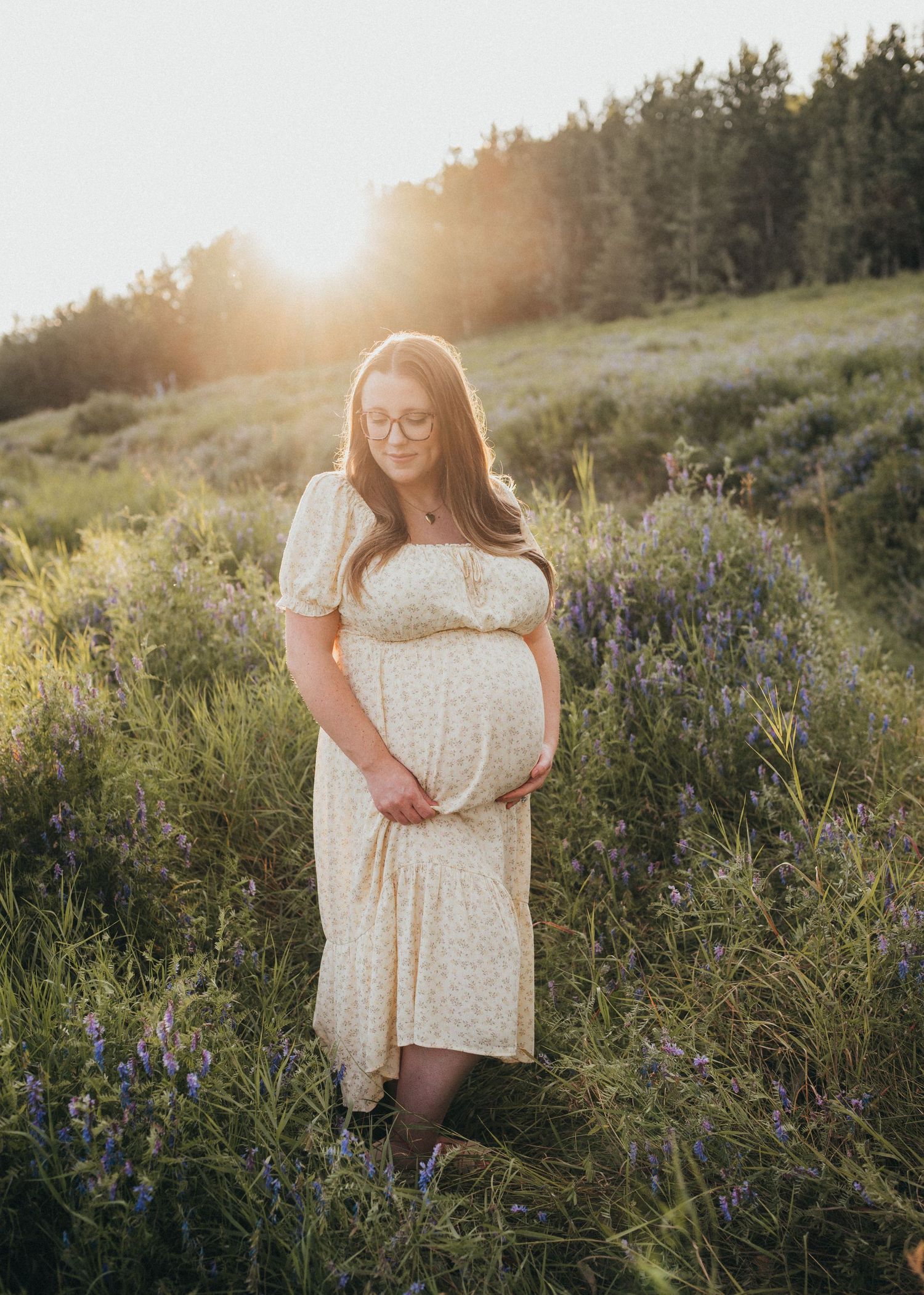 Pregnant woman standing in a field of wildflowers at sunset during an outdoor maternity session