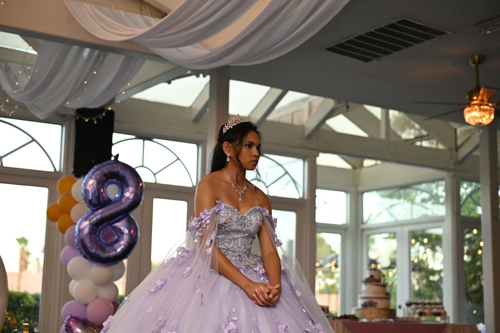 Young woman in lavender quinceañera ball gown poses elegantly at her celebration with balloon number 8 decor.