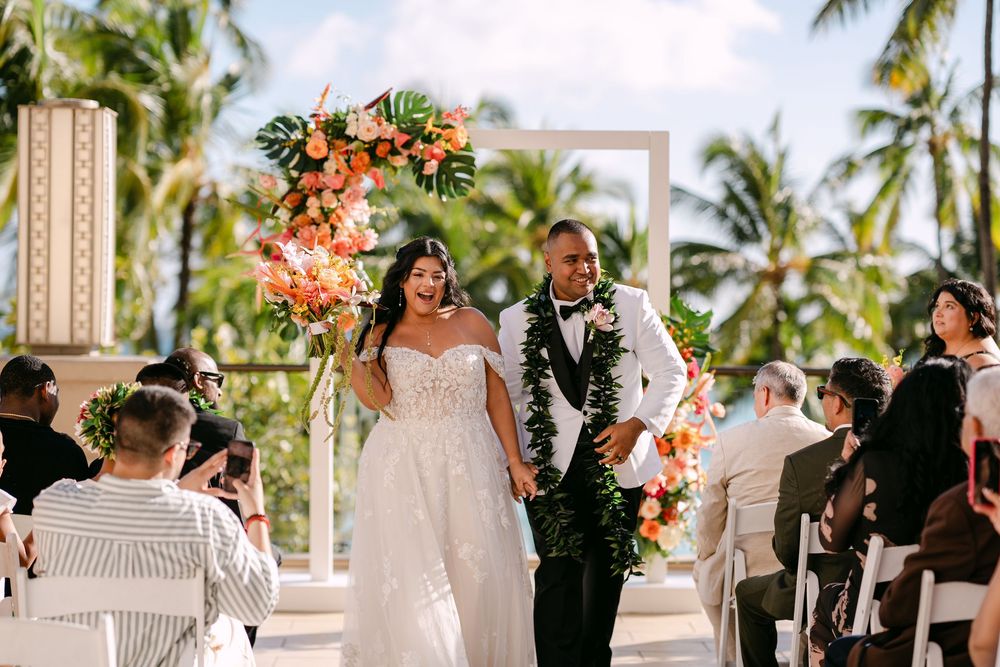 Newlywed couple walks down the aisle at an outdoor tropical wedding ceremony with floral arch.