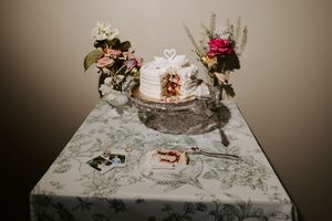 Elegant wedding cake with swan topper on floral tablecloth, surrounded by pink and white flower arrangements.