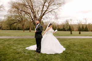 Bride and groom share a romantic first look moment on lush green lawn with bare trees in background.