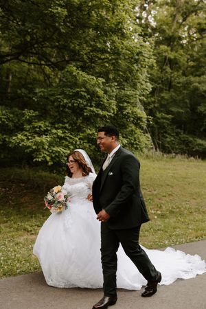 A bride in a white gown holding a bouquet walks arm-in-arm with a groom in a dark suit outdoors.