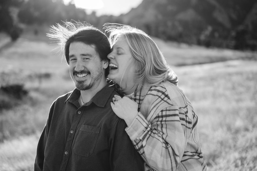 A joyful couple laughing together outdoors in a black and white photo, woman in plaid embracing man.