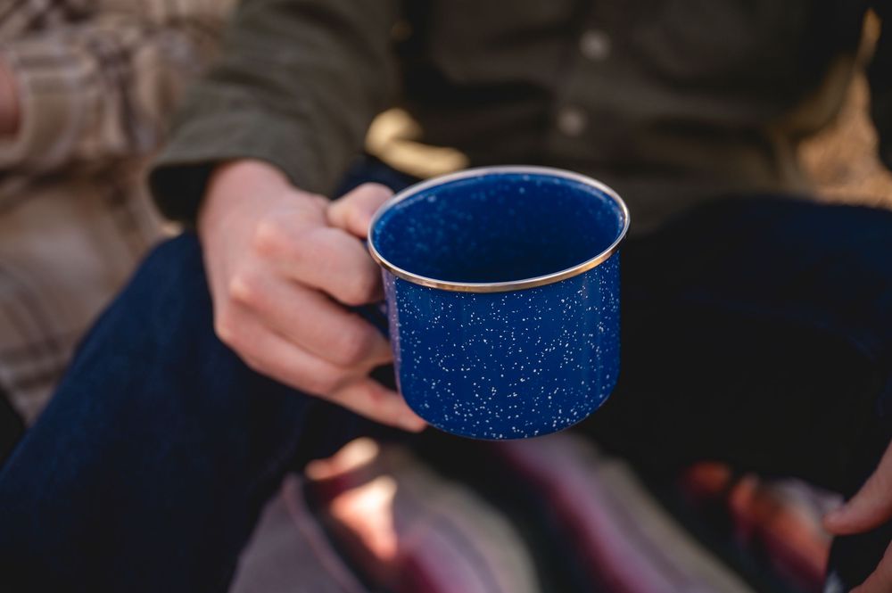 Person holding a blue speckled enamel camping mug outdoors in natural light.