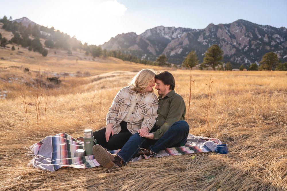 Couple sharing a romantic picnic on a blanket in golden meadow with stunning Rocky Mountain backdrop.