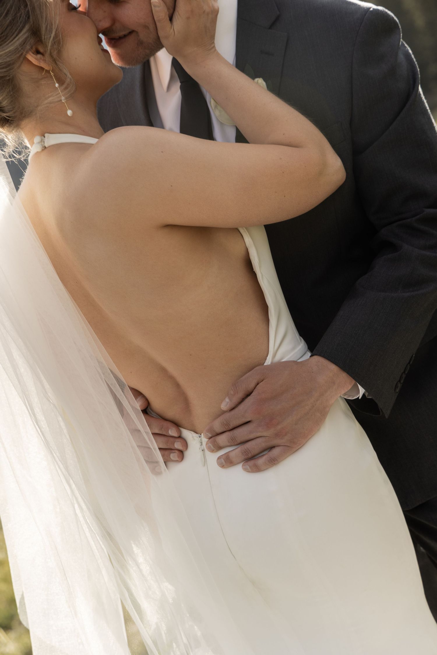 Bride and groom sharing an intimate moment, backless white wedding gown with veil, groom in dark suit.