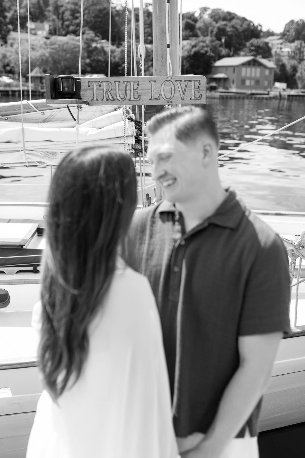 Black and white photo of couple holding hands by a True Love sailboat sign at a marina.