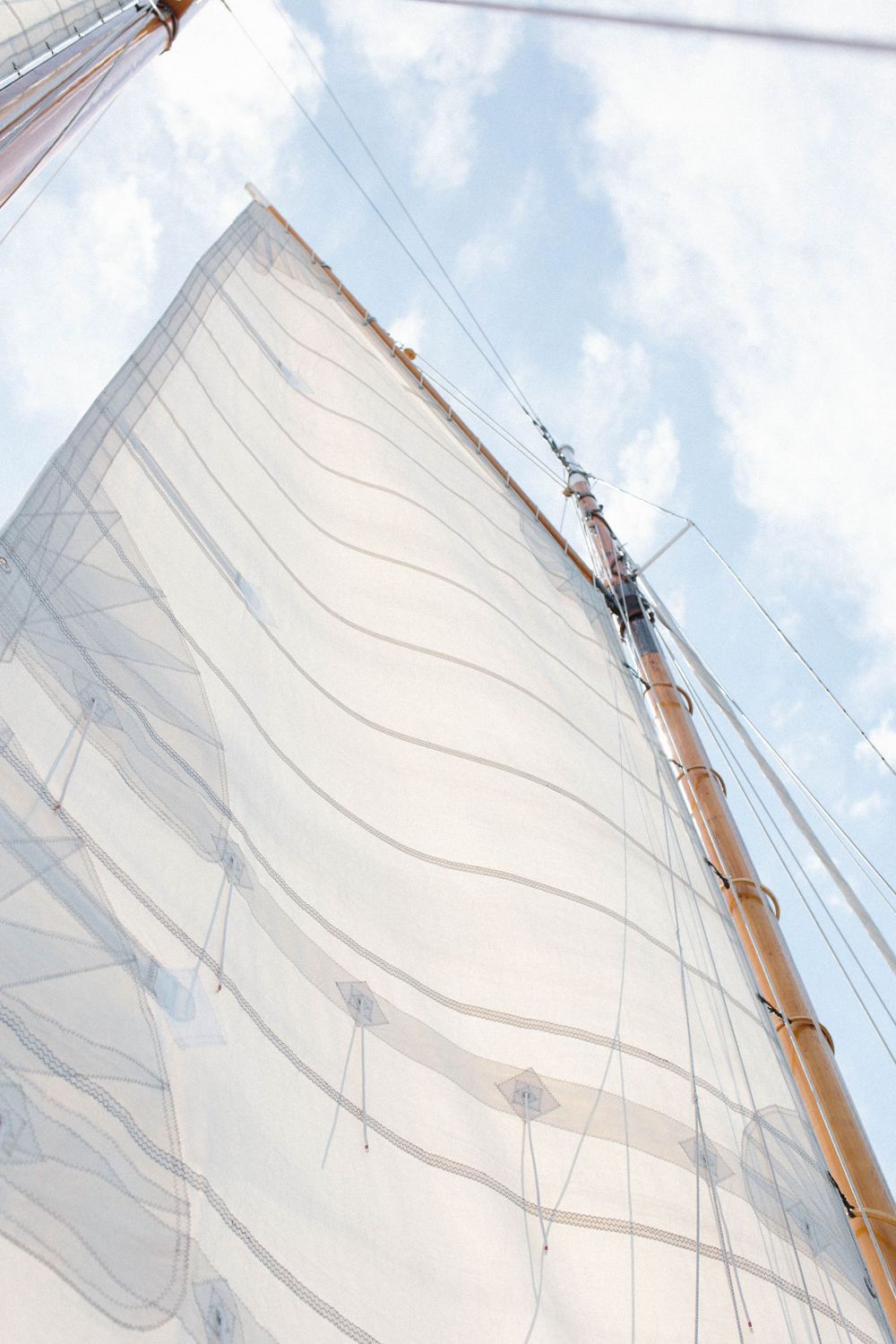 Low angle view of a white sail and wooden mast against a bright cloudy sky.