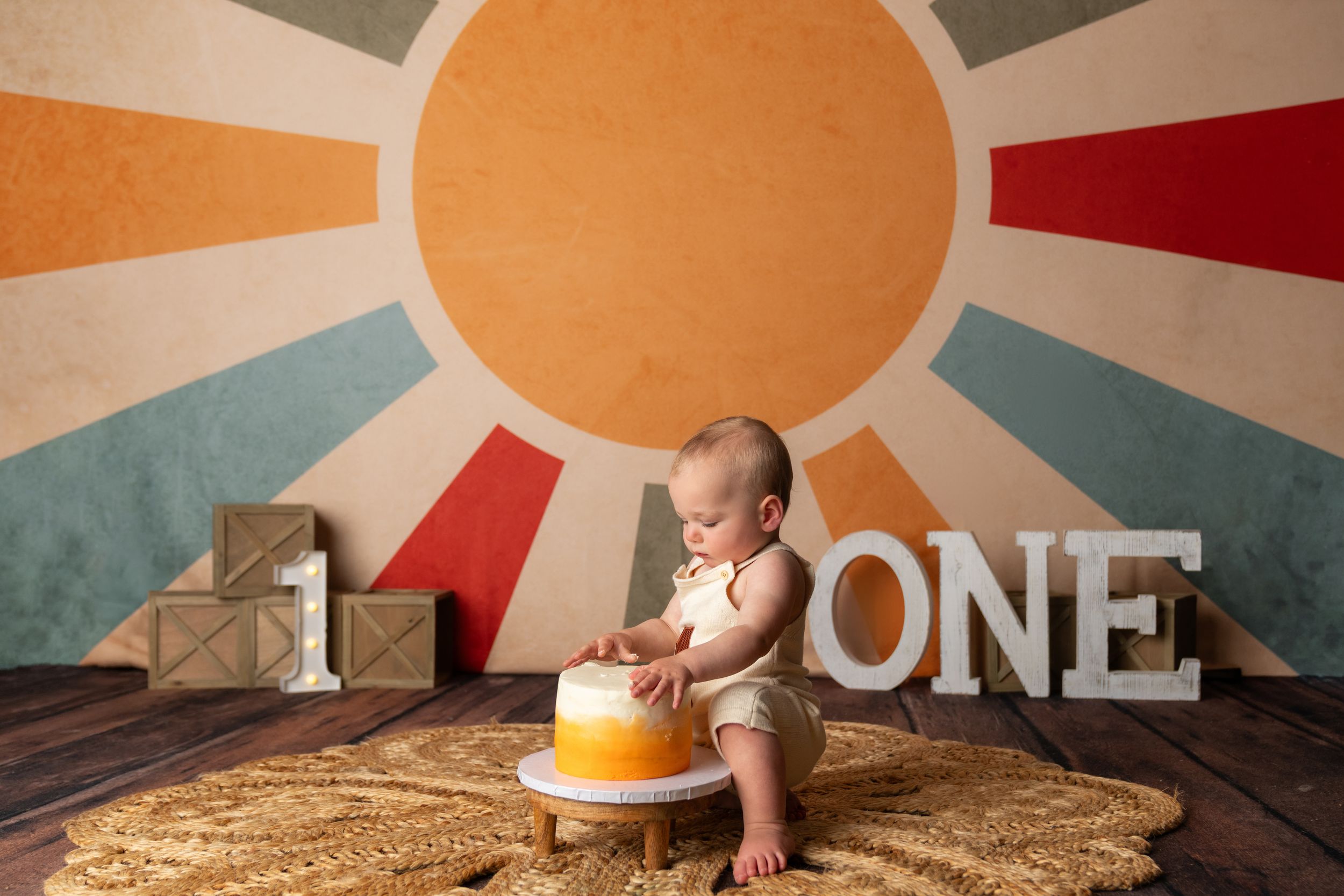Baby's first birthday cake smash photo with retro sunburst backdrop, wooden number one signs, and yellow smash cake.