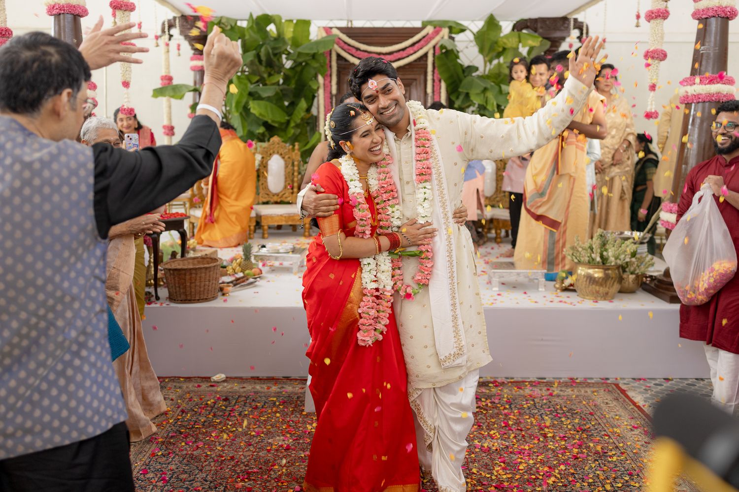 Indian bride in red saree and groom in white sherwani celebrate joyfully during traditional Hindu wedding ceremony.