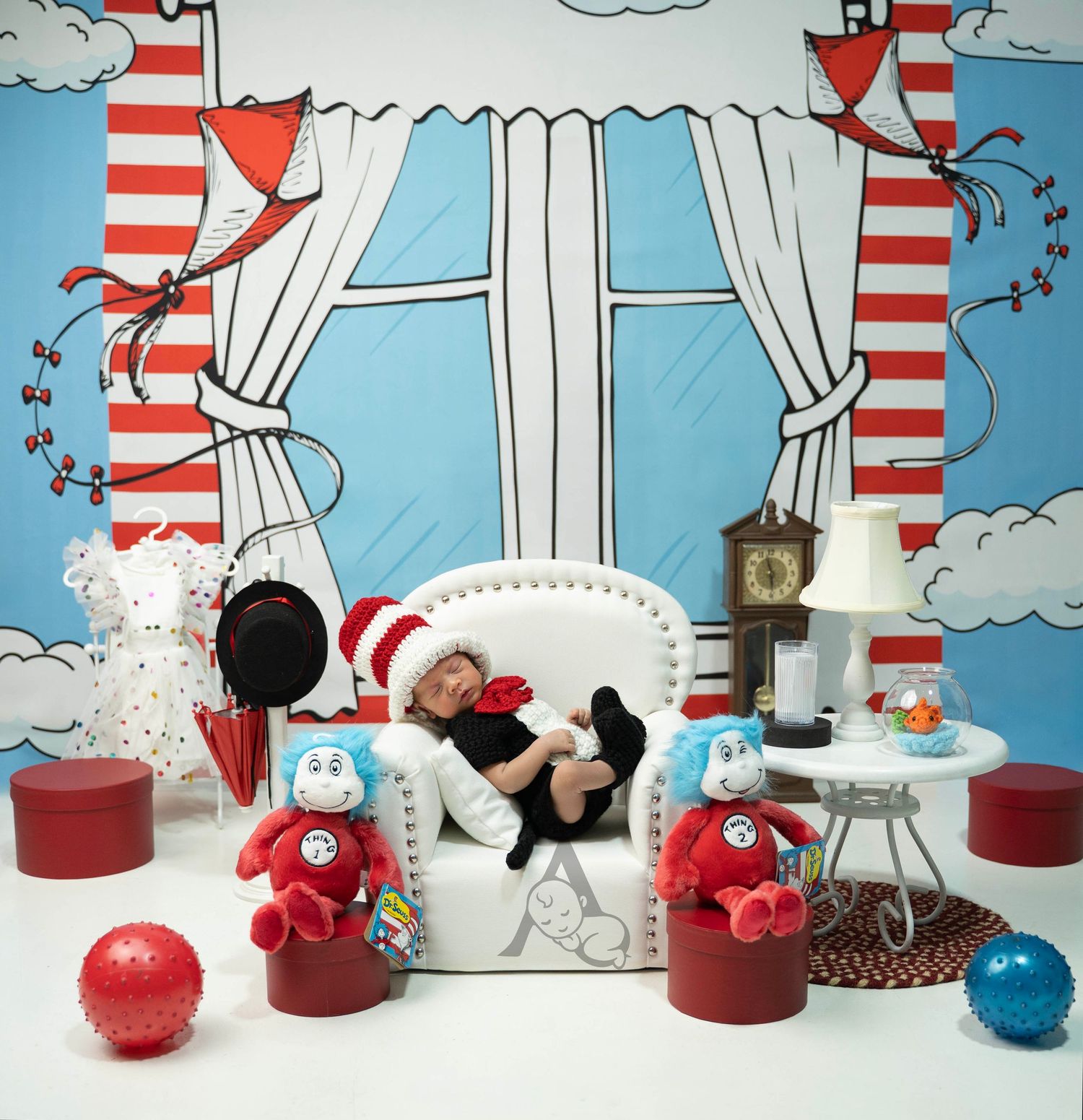 Newborn baby sleeping in white chair with Dr. Seuss Cat in the Hat themed backdrop and stuffed animals.