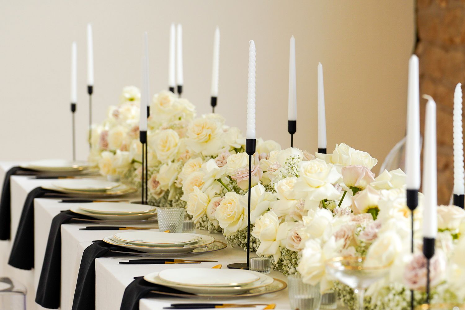 Elegant wedding reception table adorned with white roses, tall white taper candles, and black linen napkins.