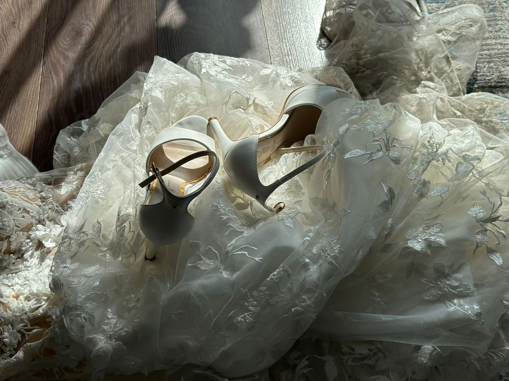 White lace wedding dress with bridal heels laid out on delicate floral fabric.