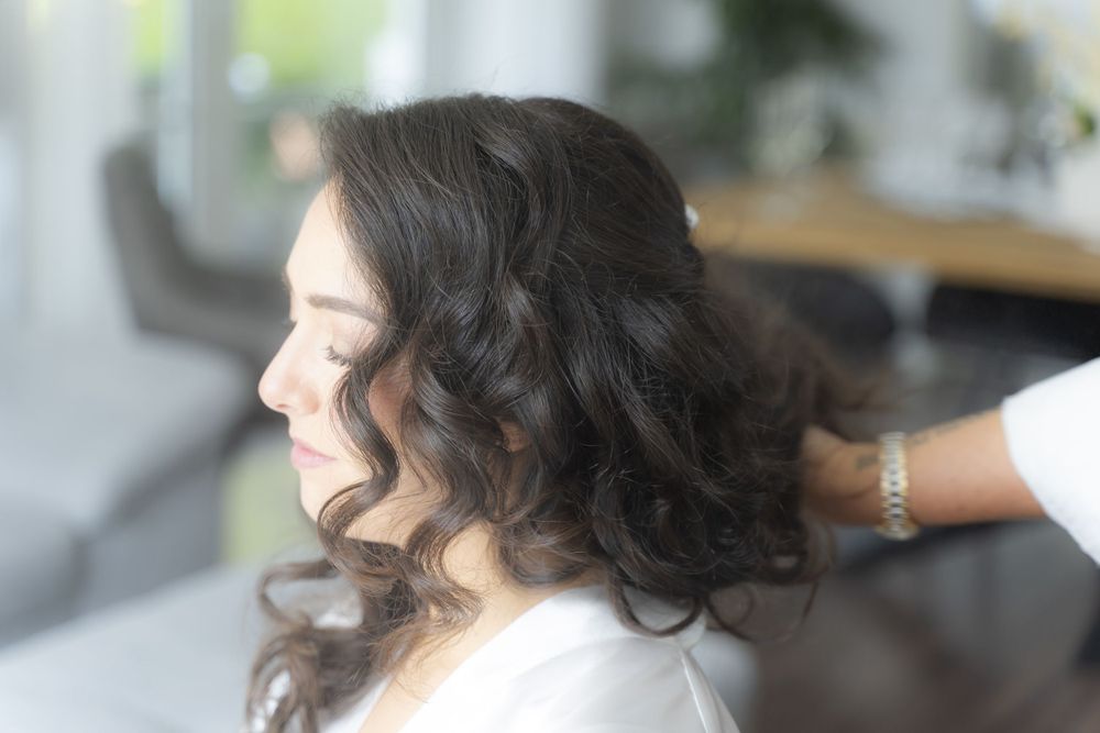Close-up of brides beautiful dark curly hair being styled by hairdresser before wedding.