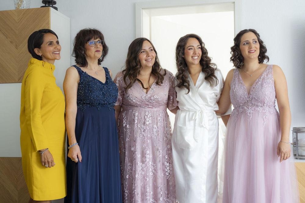 Bride with bridesmaids in colorful formal gowns smiling together before wedding ceremony.