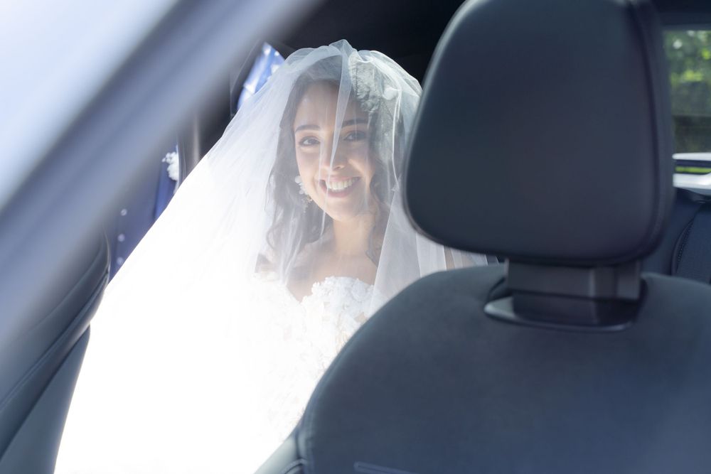 Smiling bride in white veil and gown seated in car on wedding day.