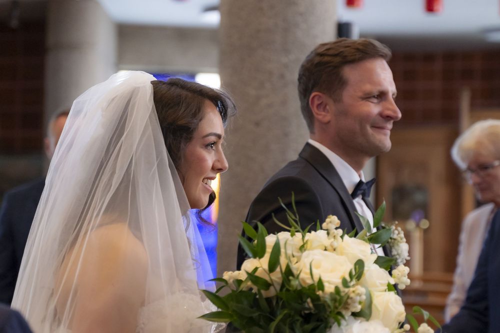 Bride holding white bouquet and groom in tuxedo smiling during wedding ceremony.