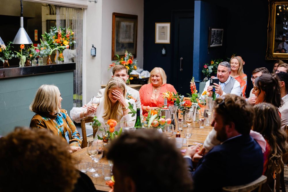 Guests laughing and toasting at a vibrant indoor dinner party with colorful floral centerpieces.