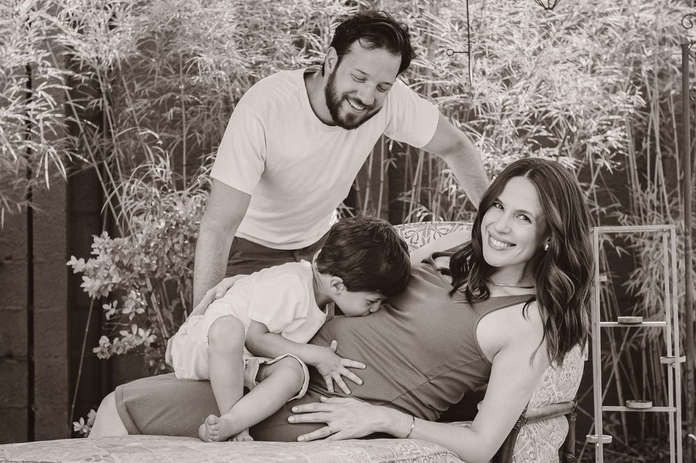 Black and white family maternity photo with pregnant woman, man, and child posing together outdoors.