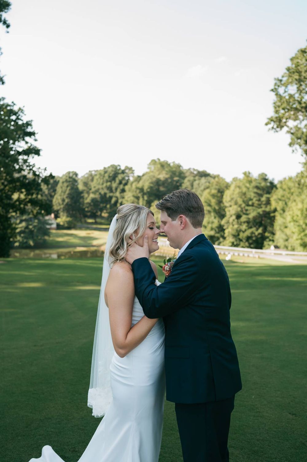 Bride and groom share a romantic moment on a lush green golf course, with the bride in a white gown and veil.