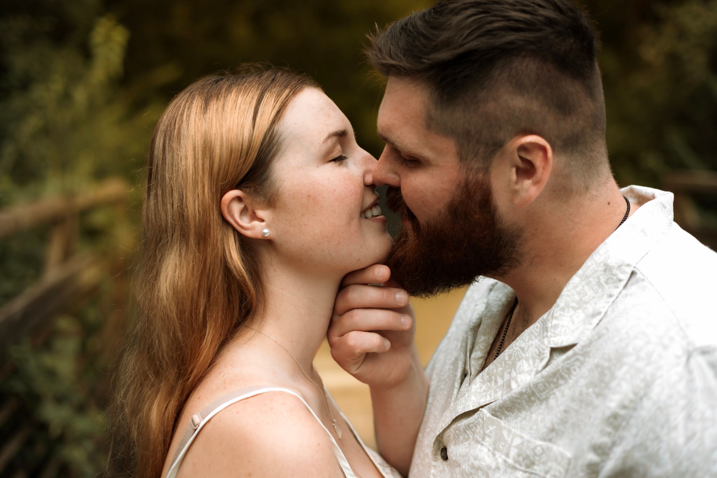 A couple sharing a tender romantic moment outdoors, with the man gently holding the woman's chin.