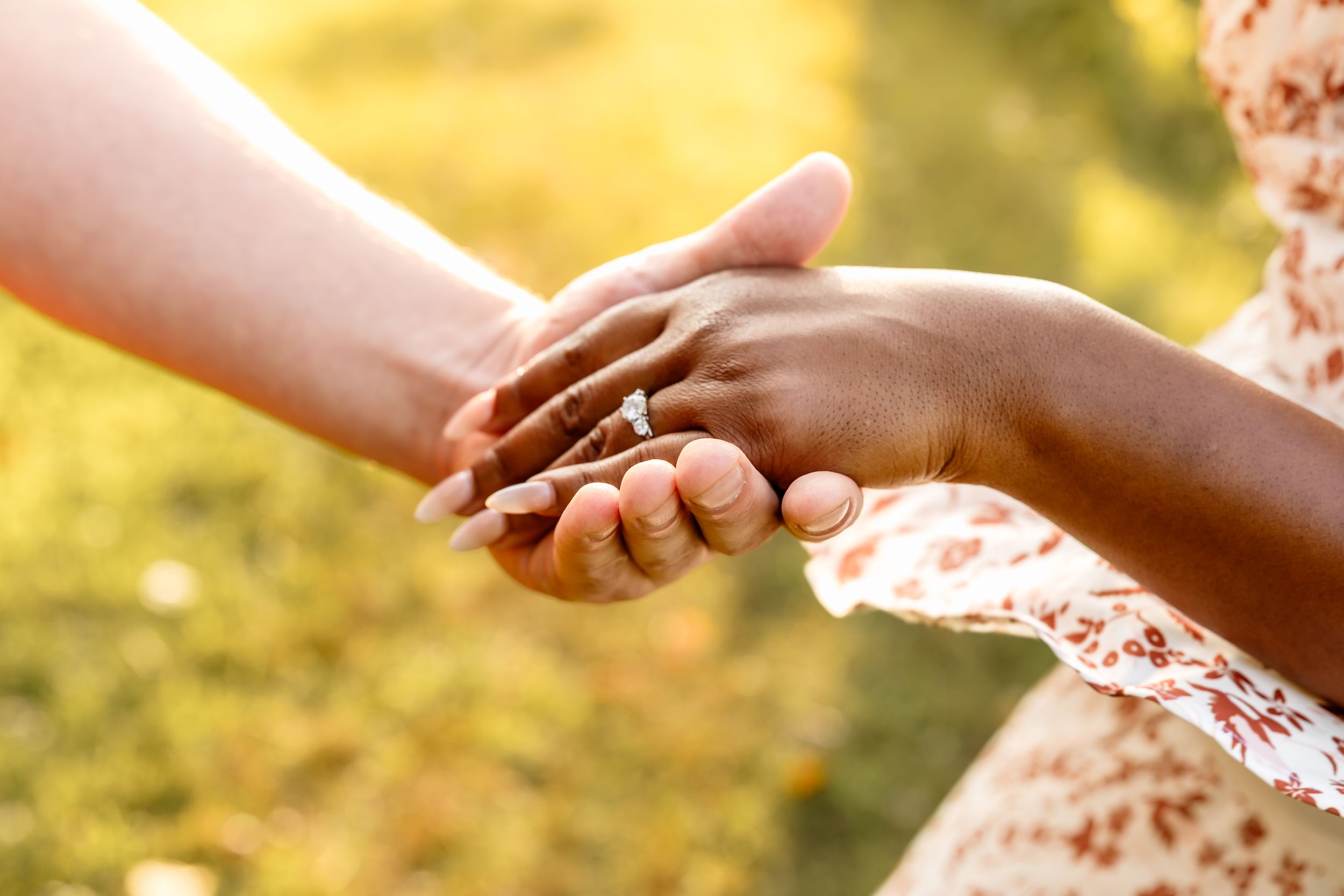 Two women of different ethnicities holding hands outdoors, symbolizing unity and friendship in warm sunlight.