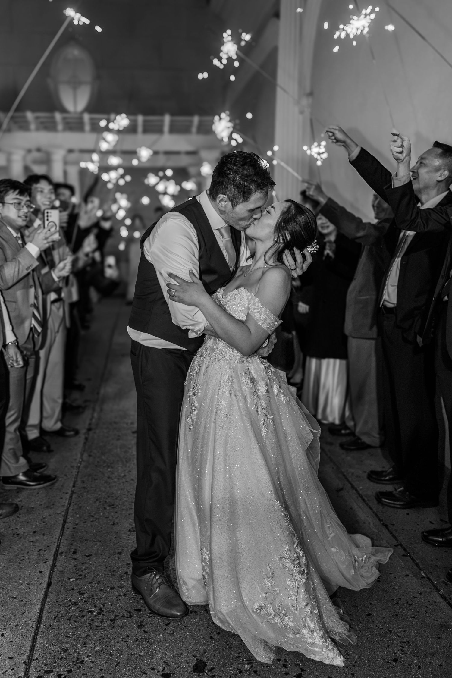 Black and white photo of a bride and groom kissing during a sparkler send-off at their wedding reception.