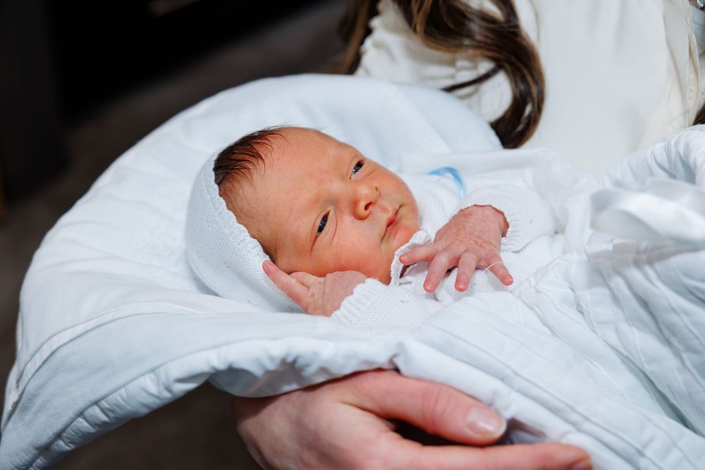 Newborn baby wrapped in white blanket cradled in mother's arms after birth.