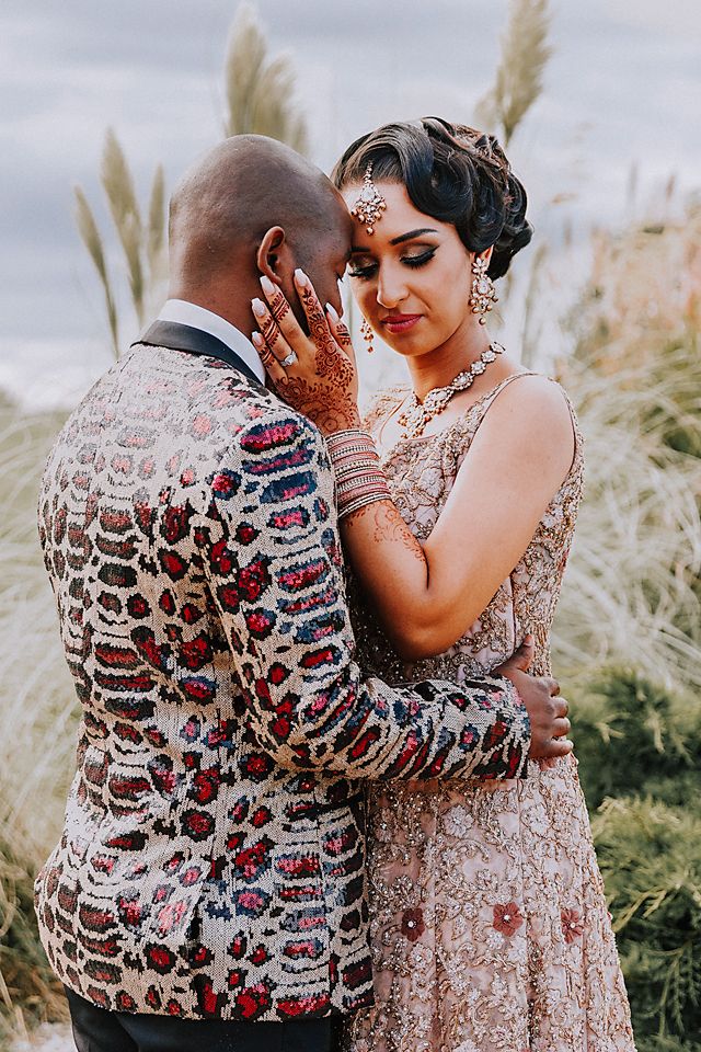 A romantic couple in wedding attire embraces outdoors with pampas grass in the background during a golden hour photoshoot.
