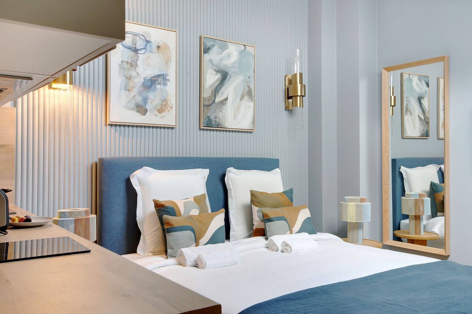 Elegant blue bedroom with gold wall sconces, decorative pillows, and a full-length mirror.