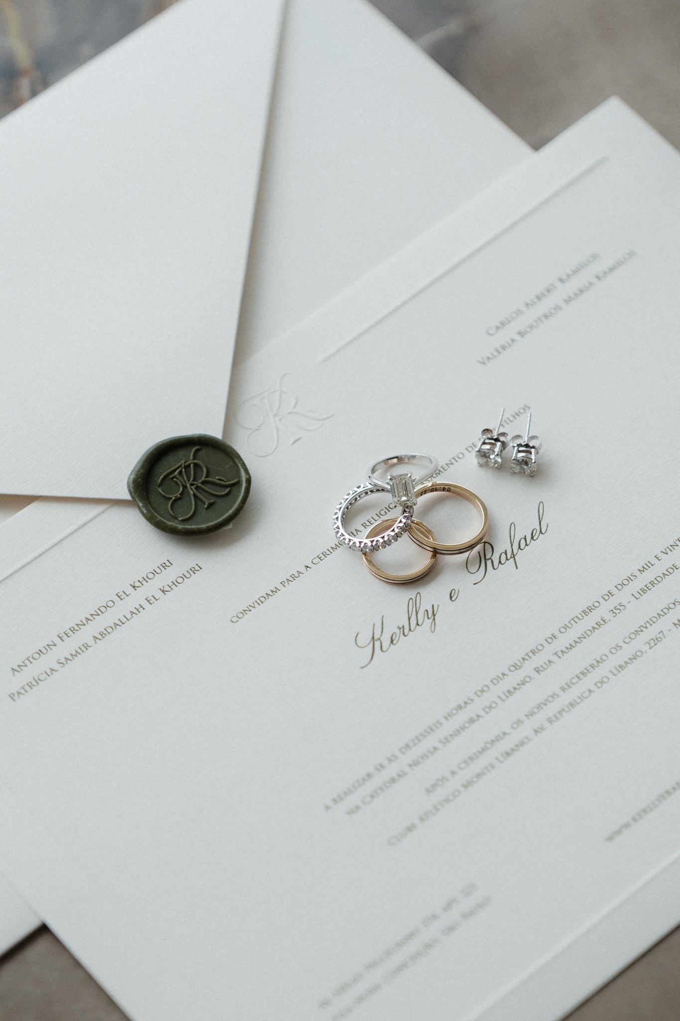 Elegant wedding invitations with wax seal and diamond rings displayed on white paper.