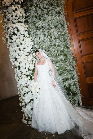 A stunning white wedding gown with a flowing train is showcased against a backdrop of white floral arrangements.