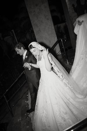 A black and white photo series showing a bride in a flowing lace wedding dress walking down dark stairs.