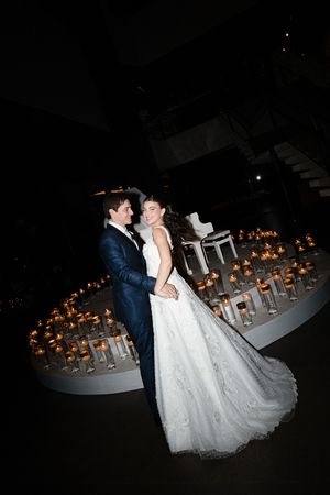 A couple in wedding attire shares a romantic dance at night with glowing candles lining the dance floor.