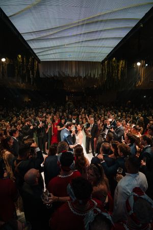 Large crowd of wedding guests dancing and celebrating on a dance floor at an evening reception under white tent lighting.