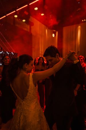 A couple dances intimately at a wedding reception under dramatic red lighting while guests watch in the background.