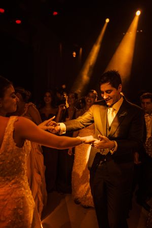 A couple dances together at their wedding reception under dramatic amber spotlights in a darkened venue.