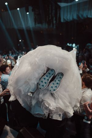 A white wedding dress with polka dot shoes peeks out from underneath at a dimly lit concert venue.
