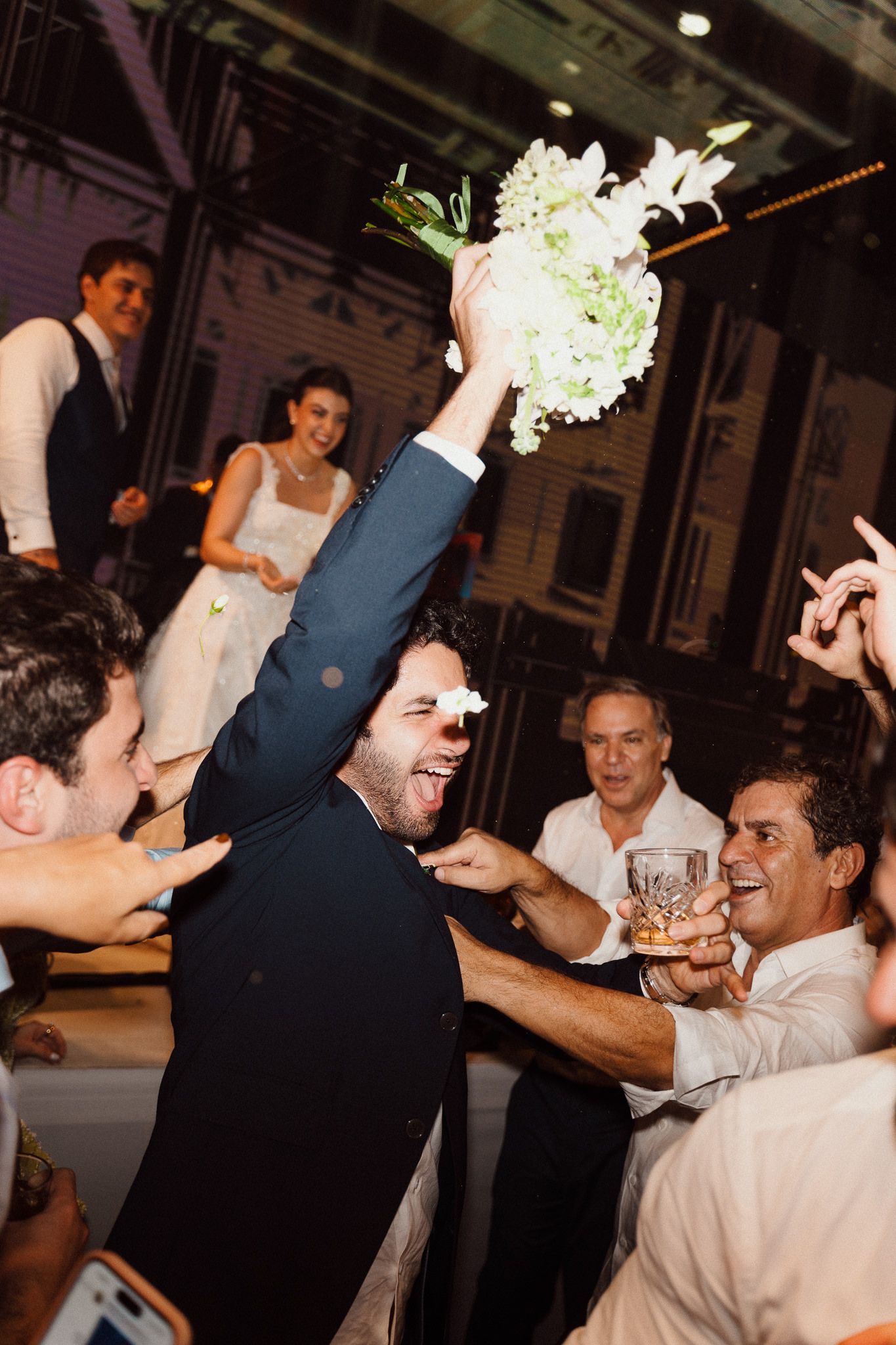 Wedding guests celebrate and dance together during a joyful reception party on a dimly lit dance floor.