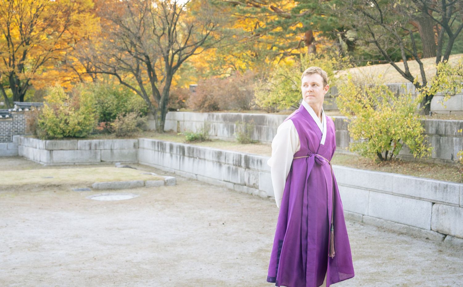 A person in a flowing purple dress twirls gracefully in an autumn garden setting with golden foliage in the background.