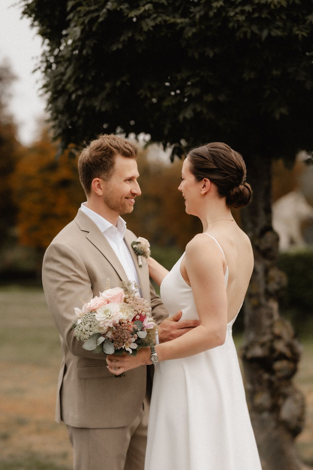 A bride and groom share a joyful moment together outdoors during their autumn wedding celebration.