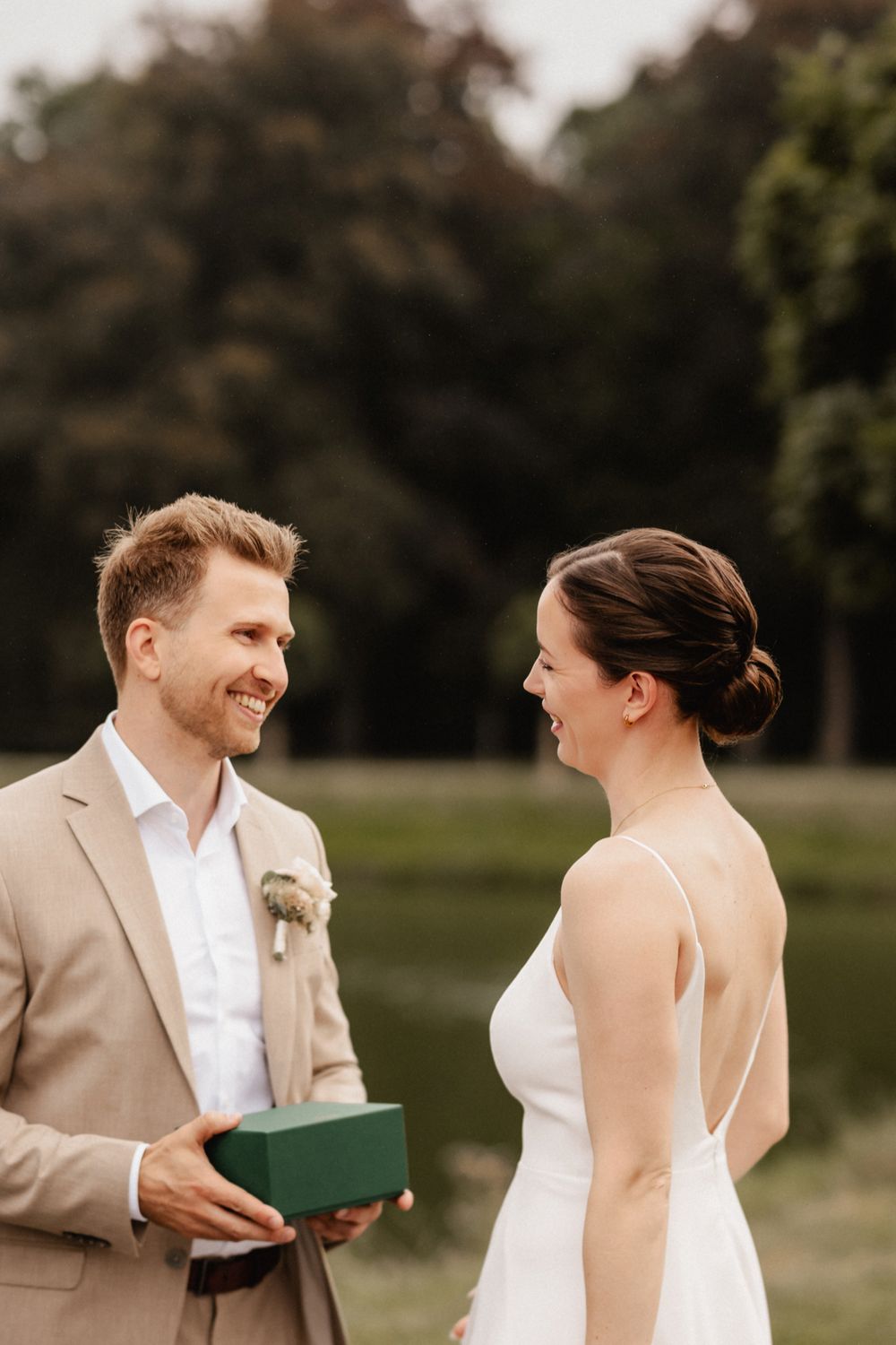 Candid outdoor wedding moment showing couple laughing while holding papers in a garden setting.